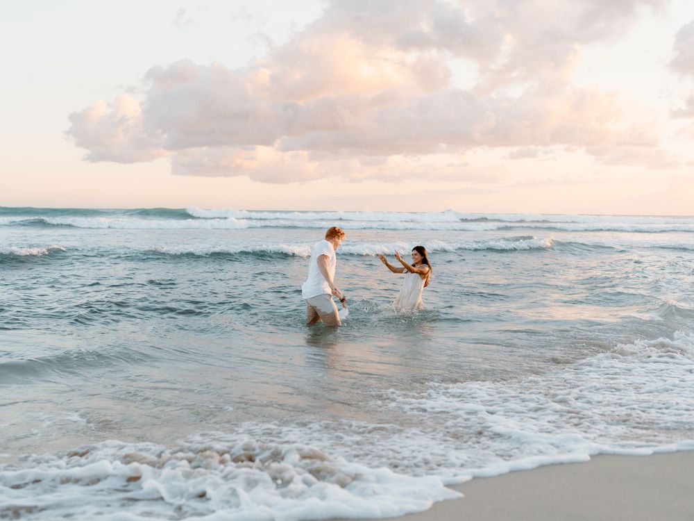 A couples photoshoot by Moments With Kell on Oahu in Hawaii with husband and wife playing in the water