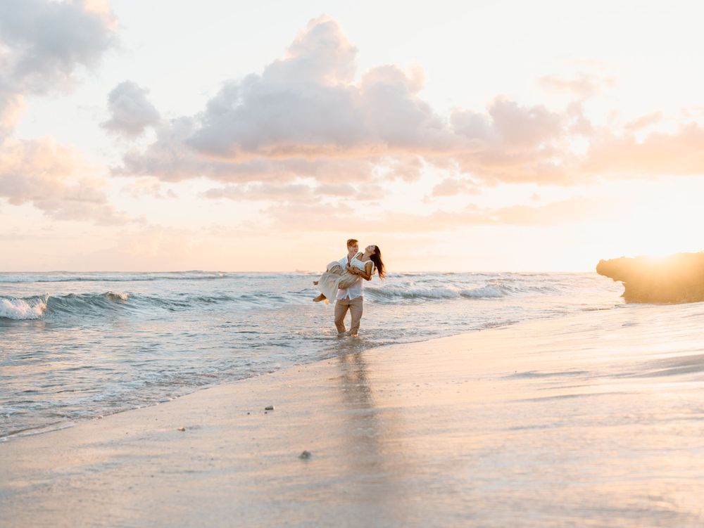 A couples photoshoot by Moments With Kell on Oahu in Hawaii with husband carrying wife on the water and sand