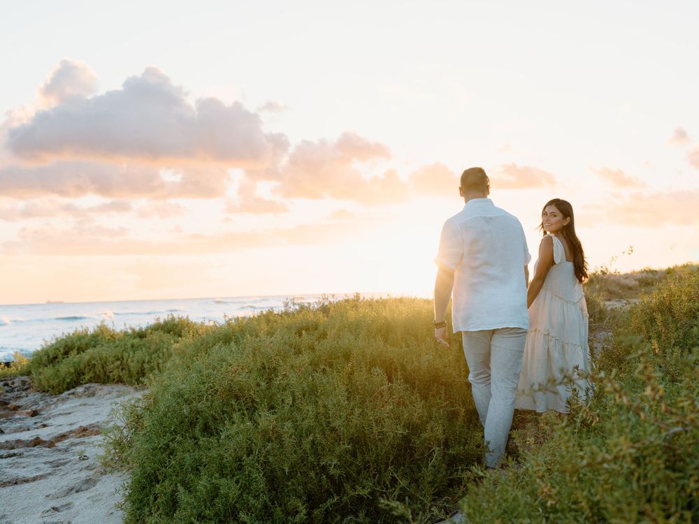 A couples photoshoot by Moments With Kell on Oahu in Hawaii with husband and wife walking hand in hand on the beach
