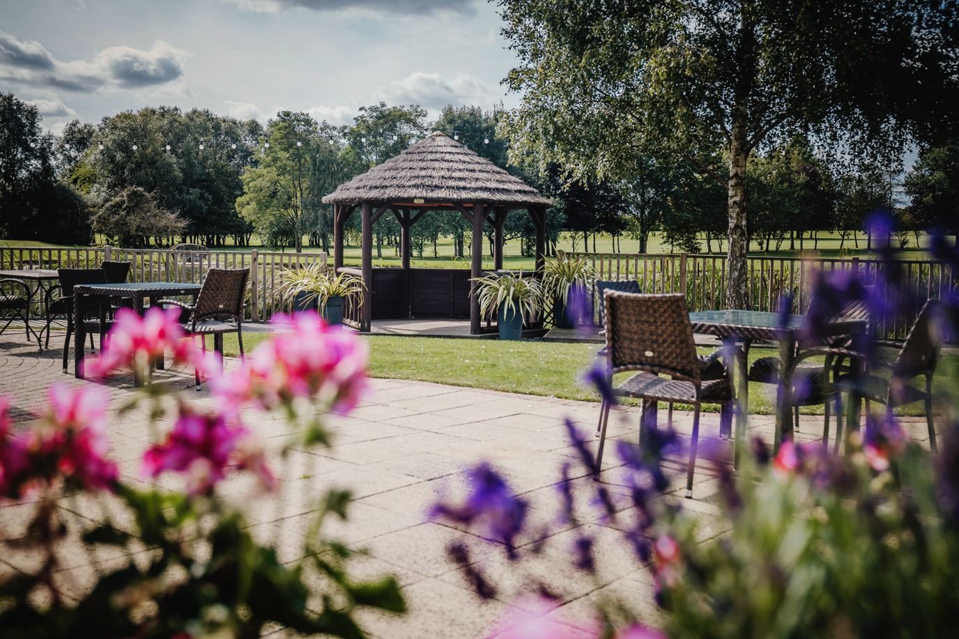 Garden gazebo surrounded by colorful flowers and outdoor seating area.