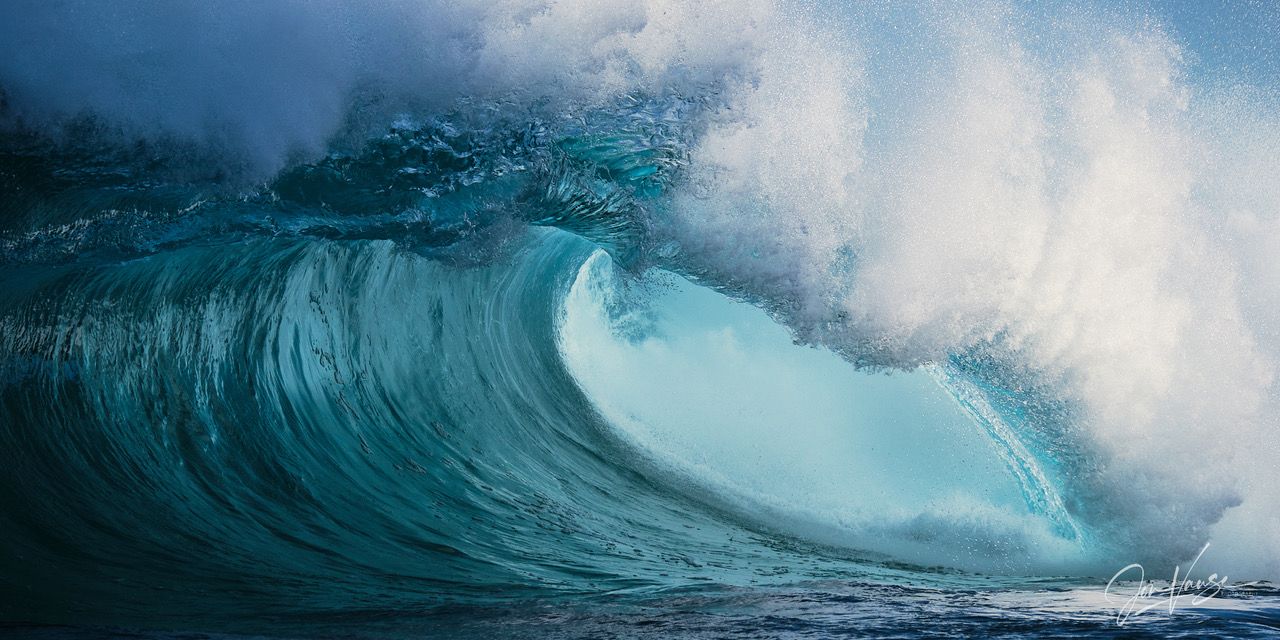 A massive turquoise ocean wave curls over with white spray in dramatic lighting.