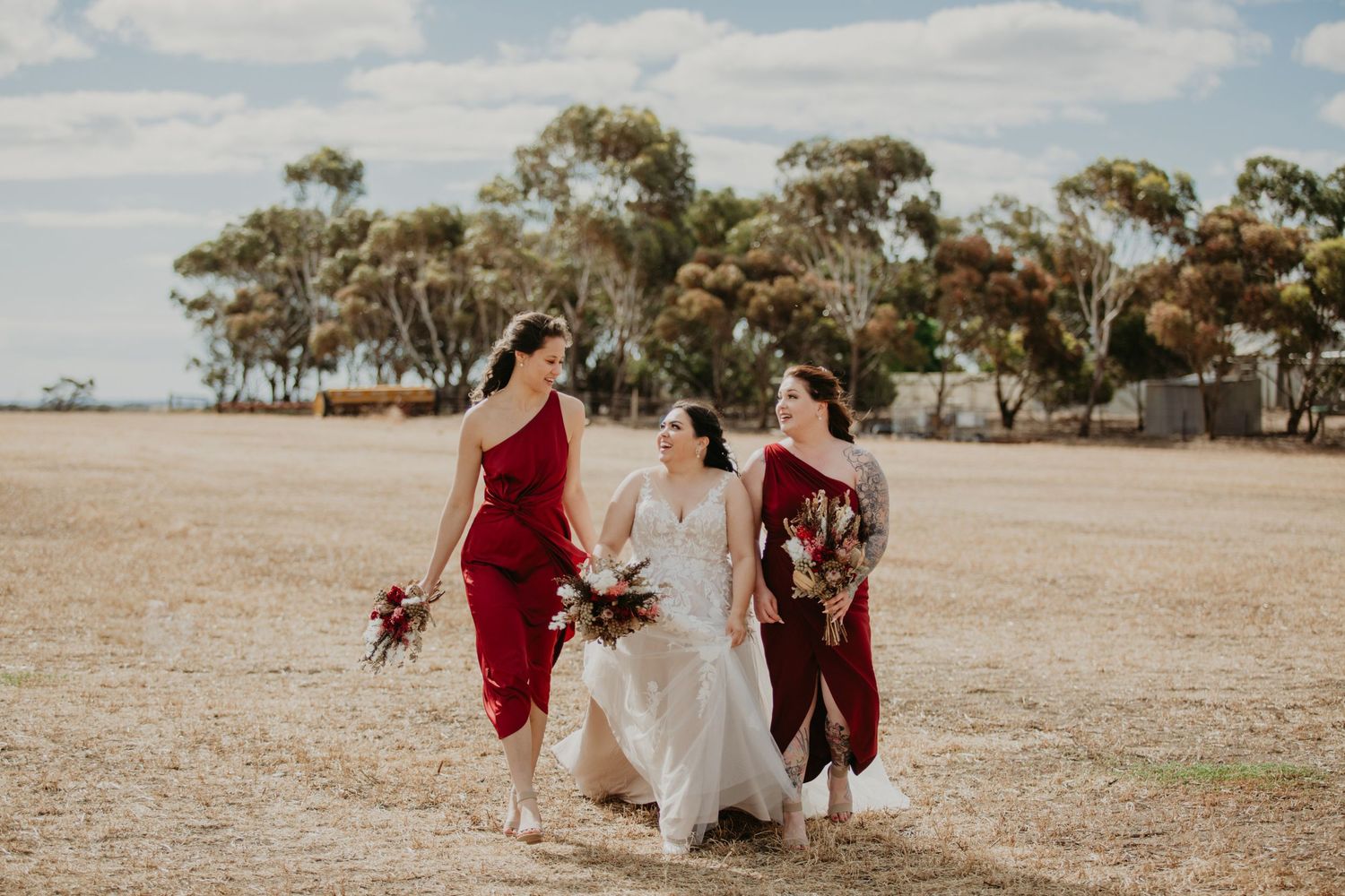 bride in white with two maroon bridesmaid dresses walking through Redwing Farm