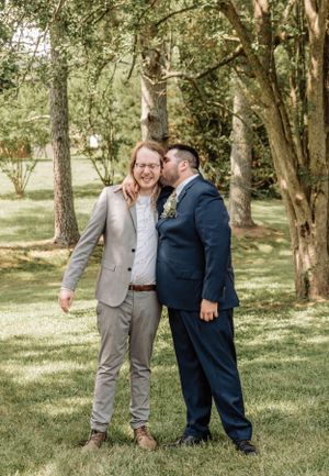Wedding party members in contrasting suits pose together on grassy lawn with trees.