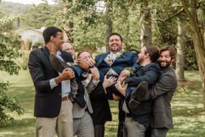 Wedding party members laugh together during a casual outdoor photo session in a wooded area.