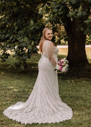 Wedding dress with intricate lace details and flowing train photographed in a garden setting.