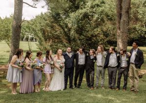 Elegant wedding party lineup with bridesmaids in lavender and groomsmen in dark suits outdoors.