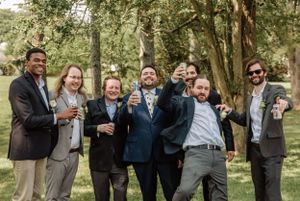 Groomsmen share genuine laughter during informal photo session in a park.