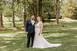 A couple stands together for their wedding portrait in a scenic wooded setting.