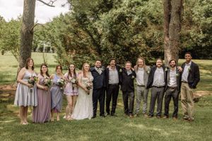 Wedding group stands in formation on grassy lawn with trees creating natural backdrop.