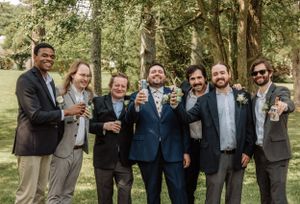 Wedding party members gather for casual group photos while celebrating outdoors among trees.