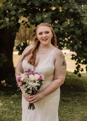A person wearing a white lace wedding gown holds a beautiful bouquet of pink and white flowers.