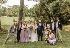 Wedding party poses playfully for group photos in a scenic outdoor garden setting.