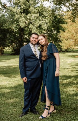 Outdoor wedding portrait with couple in coordinating navy formal wear under trees.