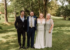 Wedding party members pose together on grassy hillside with trees in background.