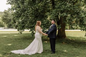 A couple shares a tender moment during their wedding ceremony under a large tree in a park setting.
