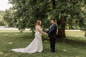 A couple exchanges vows during an intimate outdoor wedding ceremony beneath leafy green trees.