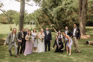 Fun wedding party photo with group showing excitement and movement under trees.