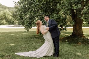 A romantic wedding photo of a couple in formal attire sharing an intimate moment under a tree.