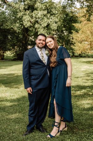 Wedding couple poses together outdoors with one in navy suit and other in navy dress.