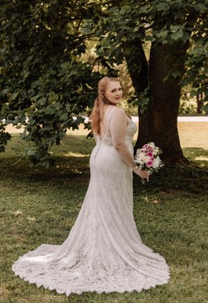 Beautiful lace wedding gown with a sweeping train displayed against a natural outdoor backdrop.