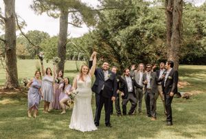 Festive wedding party gathering for group photos in natural outdoor setting.
