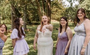 Bridal party in lavender and gray dresses poses together on a sunny day in a park setting.