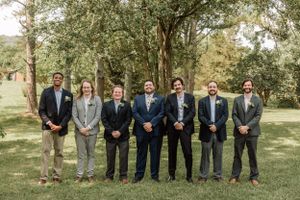 Groomsmen in dark suits and gray attire lined up for formal wedding photos outdoors.