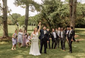 Wedding group arranges for creative photo composition in park setting.