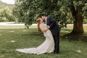 Romantic wedding couple sharing a dip kiss in a lush garden setting with flowing white dress and black suit.