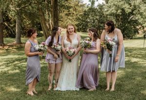 Bridesmaids in lavender dresses pose with bouquets in a sunny garden setting.