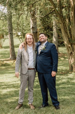 Three members of a wedding party pose casually together in a wooded outdoor setting.