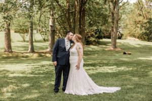 A couple embraces during their wedding photos in a sunlit wooded area.