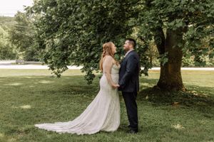 A beautiful outdoor wedding ceremony takes place on a sunny day under sprawling tree branches.