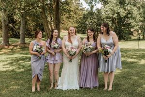 Bridal party in purple tones poses for casual photos on sunny lawn.