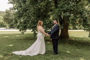 A romantic wedding scene unfolds beneath a majestic tree with sunlight filtering through the leaves.