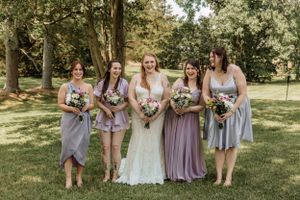 Wedding group stands together in a park wearing coordinated purple and gray attire.