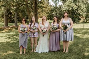 Bridal party in various shades of purple gather for photos in an outdoor garden setting.