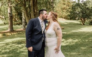 A couple laughs together during their outdoor wedding photoshoot in a wooded setting.