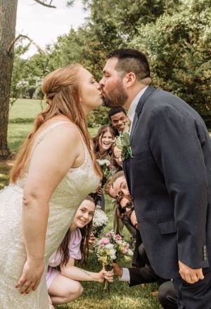 Intimate wedding moment captured outdoors with guests reacting in background.