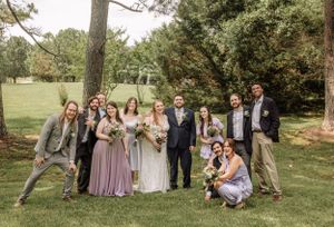 Wedding group arranges themselves casually on grassy hill for fun outdoor photography.