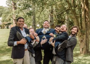 Groomsmen engage in playful photo poses while celebrating in a scenic wooded area.
