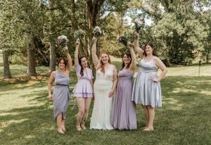 Group photo of wedding party members in pastel dresses arranged on grassy hillside.