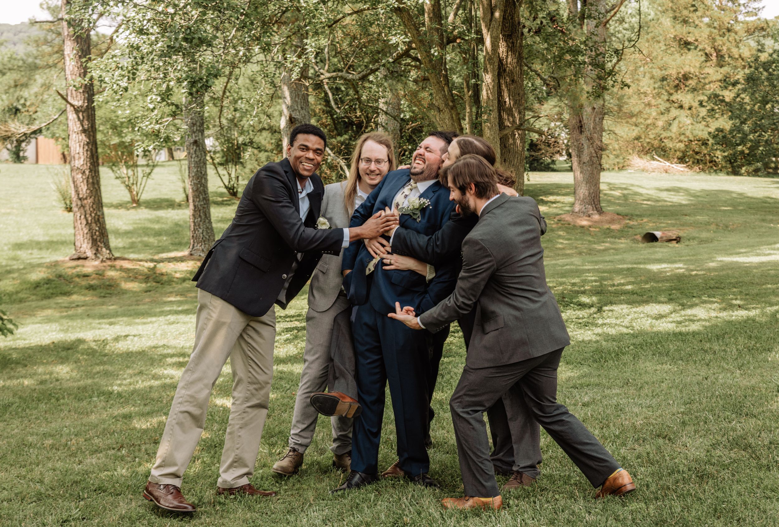 Wedding party members posing playfully together on grassy lawn.