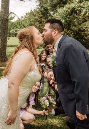 Romantic wedding kiss moment with guests celebrating in natural outdoor setting.