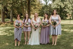 Wedding party poses casually on grass with bridesmaids in coordinated lavender dresses.