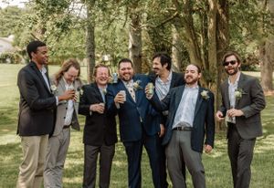 Wedding party members joke around during casual outdoor photography session under trees.