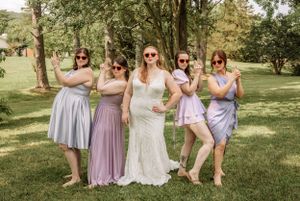 Bridal party wearing sunglasses strikes fun poses on a green lawn during summer wedding.