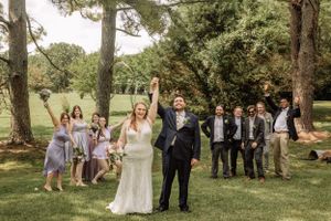 Outdoor wedding party photo session with group arranged under pine trees.