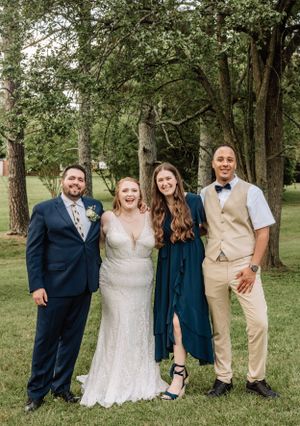 Wedding group photo with bride in white dress and guests wearing mix of navy and tan formal attire.