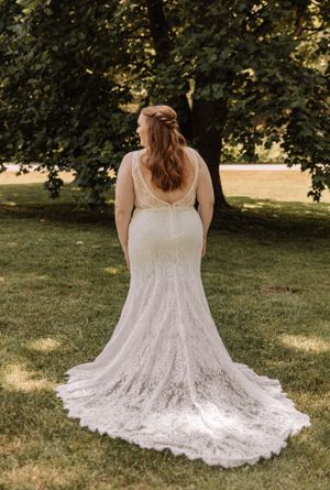 Back view of an elegant white lace wedding gown with detailed train spread out on green grass.